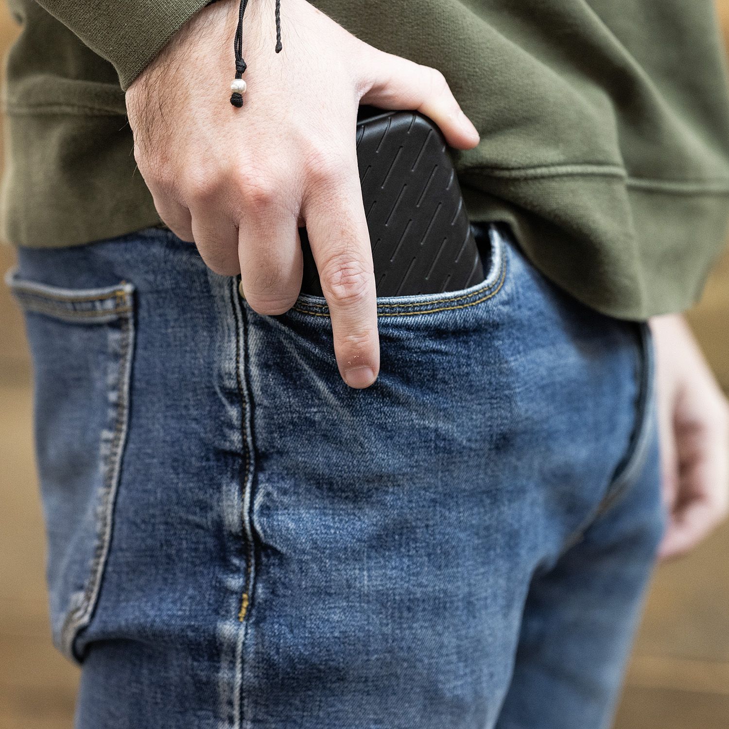 Custodia per freccette Harrows Slimcase Eine Person steckt ein schwarzes Etui in die Hosentasche. Sie trägt eine grüne Jacke und eine blaue Jeans.