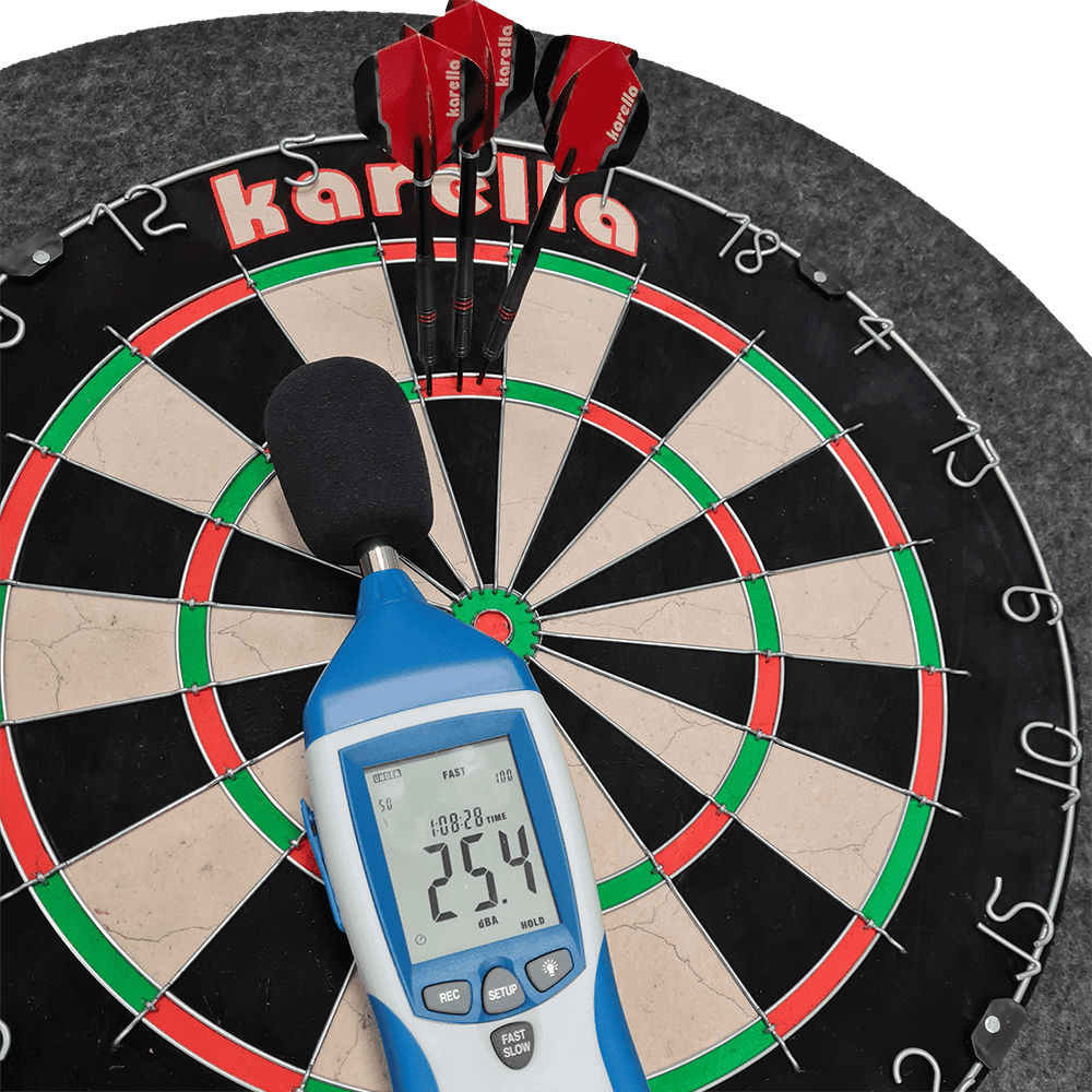 811501_Karella_Schallschutz_f-r_Steeldartboards_40AsdKuqQ3Dv9I Das Bild zeigt ein Steeldartboard mit integriertem Schallschutz und Auffangring von Karella. Auf dem Dartboard liegen drei rote Darts sowie ein Schallpegelmessgerät, das 25,4 dB anzeigt.