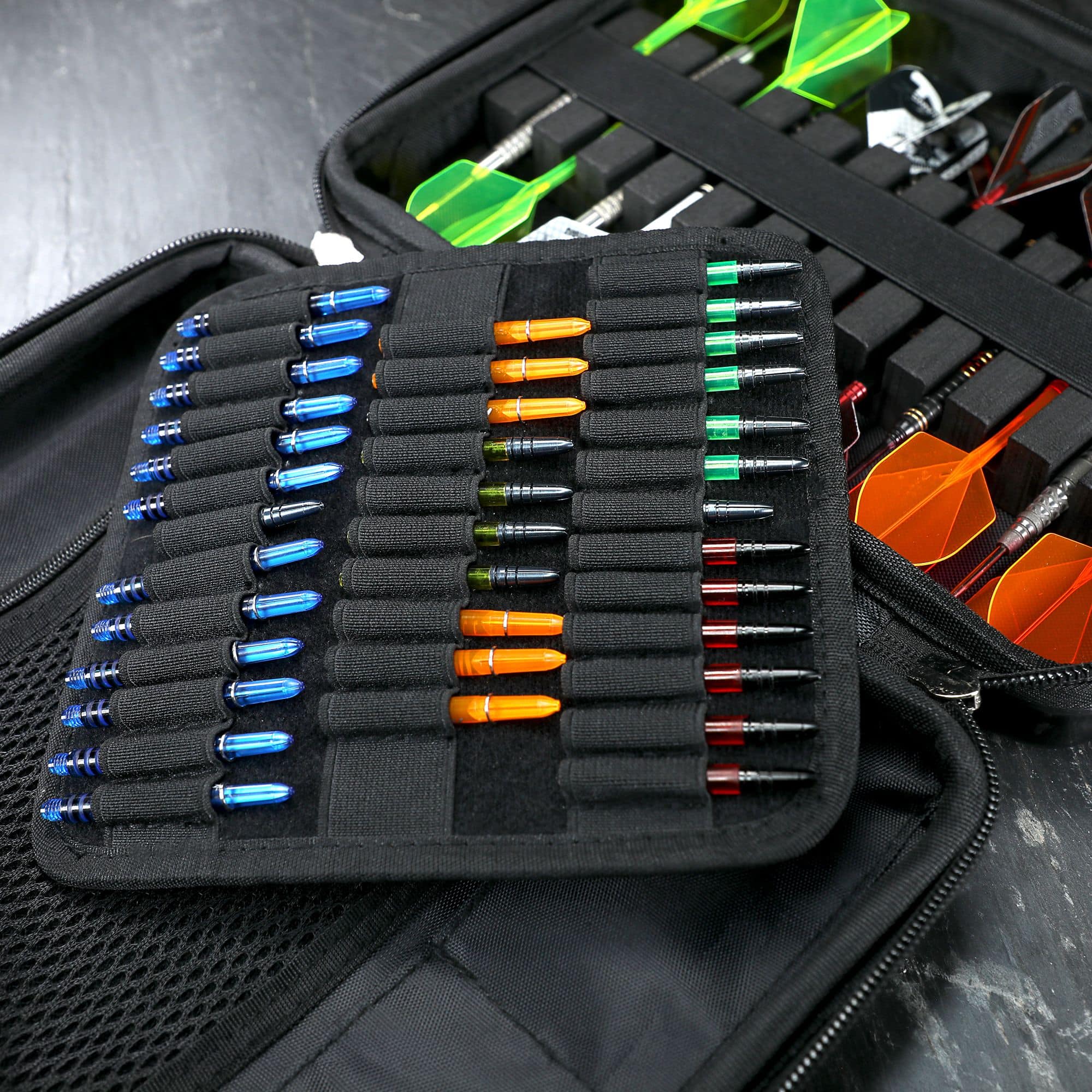 Winmau Armor G4 Dartwallet In diesem Bild ist eine geöffnete schwarze Darttasche mit vielen bunten Dartspitzen und zusammengesetzten Darts zu sehen. Die Dartpfeile und Zubehörteile sind ordentlich in verschiedenen Fächern einsortiert.