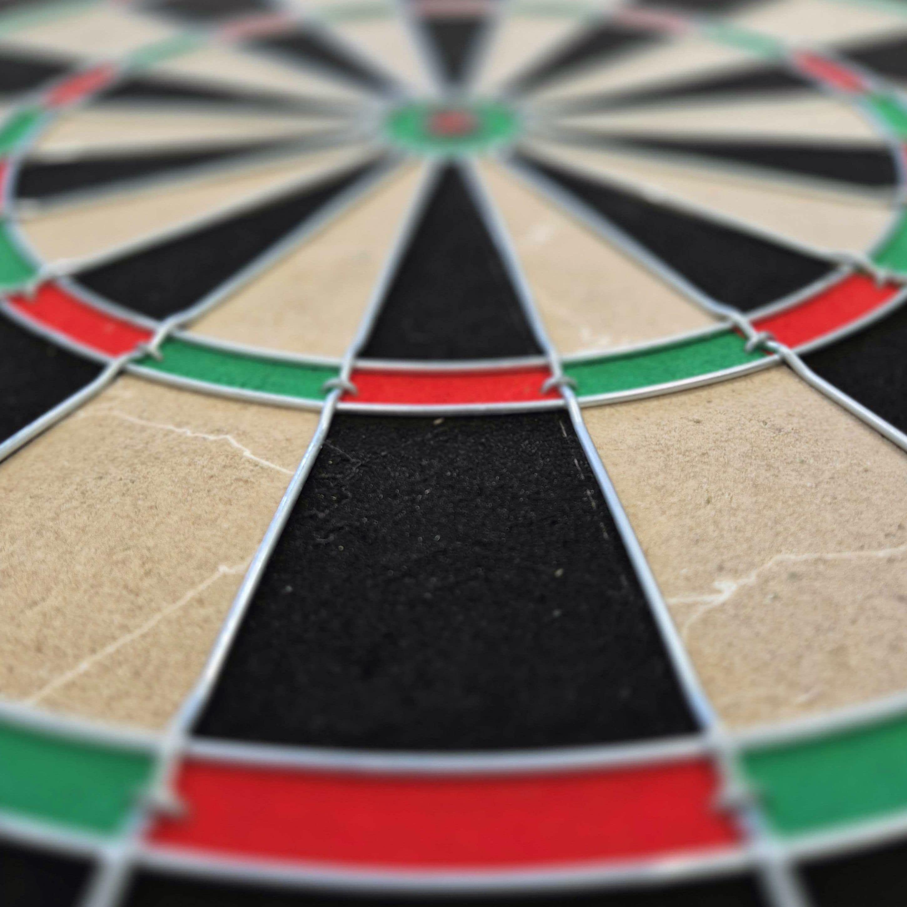 Target Dimitri Van Den Bergh steel dartboard set Das Bild zeigt eine Nahaufnahme eines Steeldartboards mit schwarz, beige, rot und grün markierten Segmenten. Besonders gut zu erkennen sind die Drähte, die die Felder voneinander trennen.