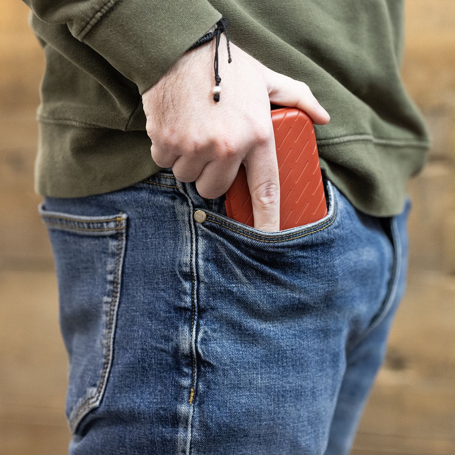 Étui à fléchettes Harrows Slimcase Eine Person steckt ein rotes Etui in die Hosentasche. Sie trägt eine blaue Jeans und einen grünen Pullover.