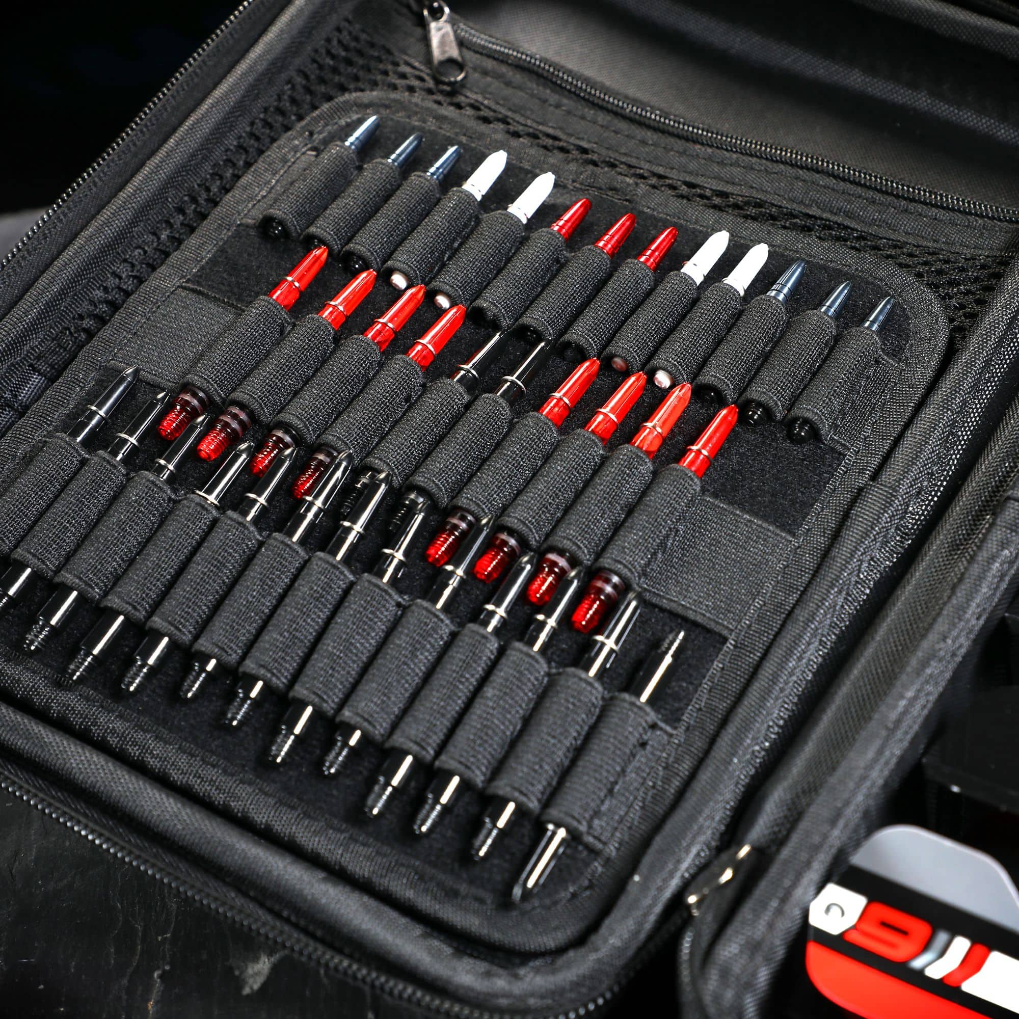 Winmau Armor G4 Dartwallet Das Bild zeigt ein geöffnetes schwarzes Dartwallet mit vielen ordentlich einsortierten Dartspitzen. Die Dartspitzen sind in elastischen Schlaufen gehalten und teilweise rot, weiß oder schwarz gefärbt.