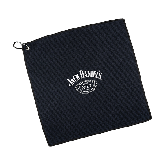 JD7032_Mission_Jack_Daniels_Handtuch_1 Dies ist ein schwarzes Handtuch mit dem weißen Jack Daniel's Logo in der Mitte. In der Ecke befindet sich eine Metallöse mit einem Haken zum Aufhängen.