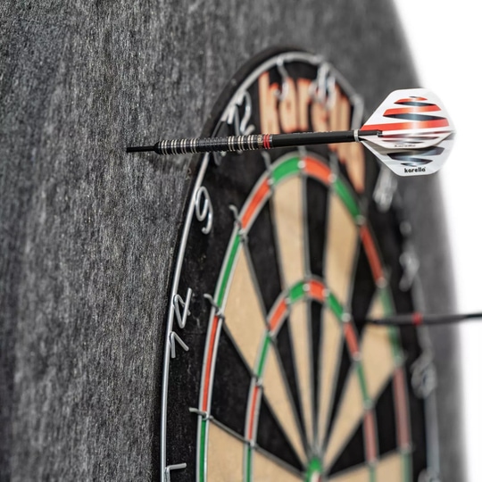 Ocelový rámeček na terč Karella Ultimo Das Bild zeigt eine Karella Ultimo Steeldartboard Surround, die einen Dartpfeil auffängt. Die graue Umrandung schützt die Wand vor Fehltreffern neben der Dartscheibe.